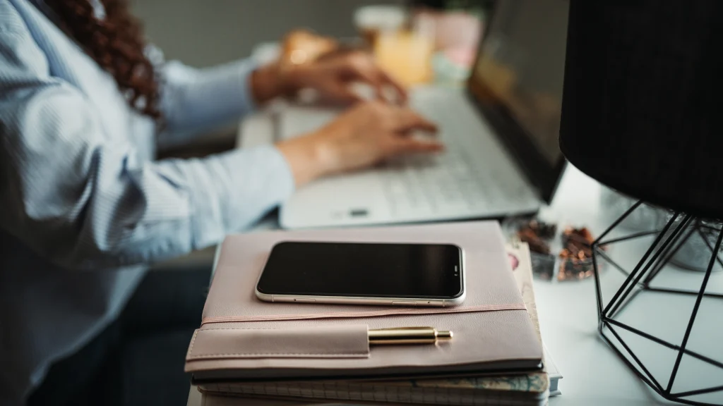 Person typing on a laptop beside a planner and smartphone in a home workspace