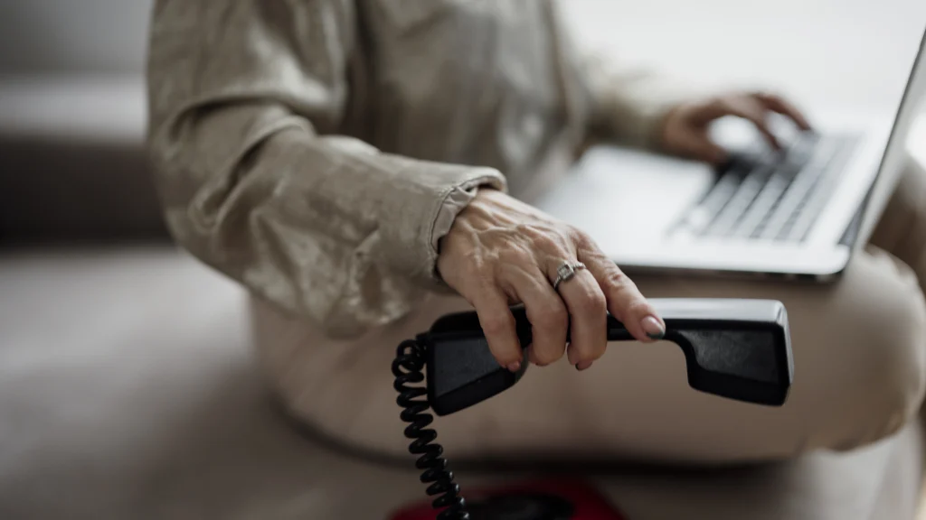 Real person working on a laptop while holding a telephone receiver