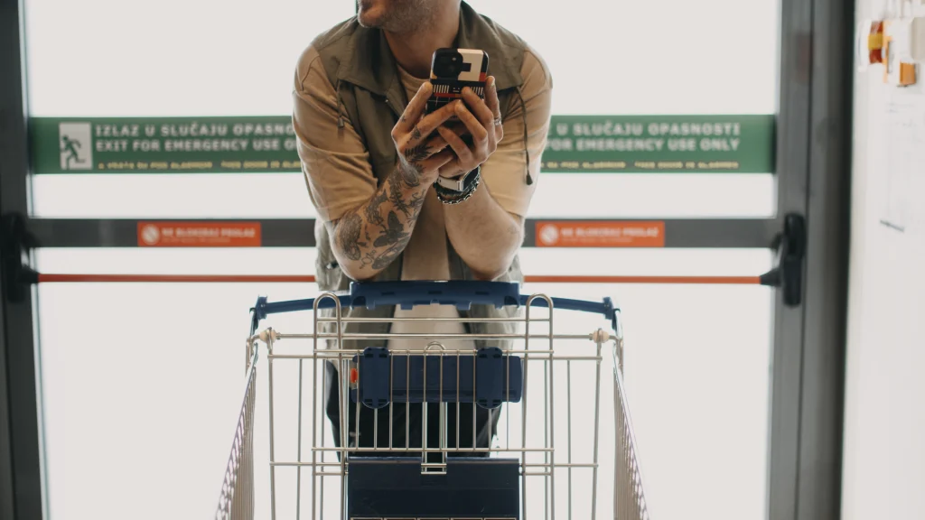Real shopper holding a smartphone behind a metal shopping cart