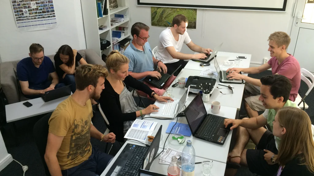 Real group of people working together around tables with several laptops